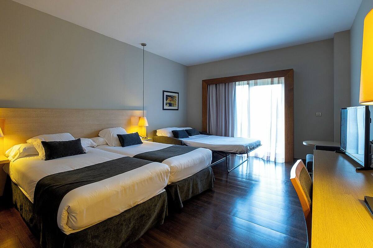 Een hotelkamer met twee bedden, een bureau, een stoel, een televisie en een raam met gordijnen.