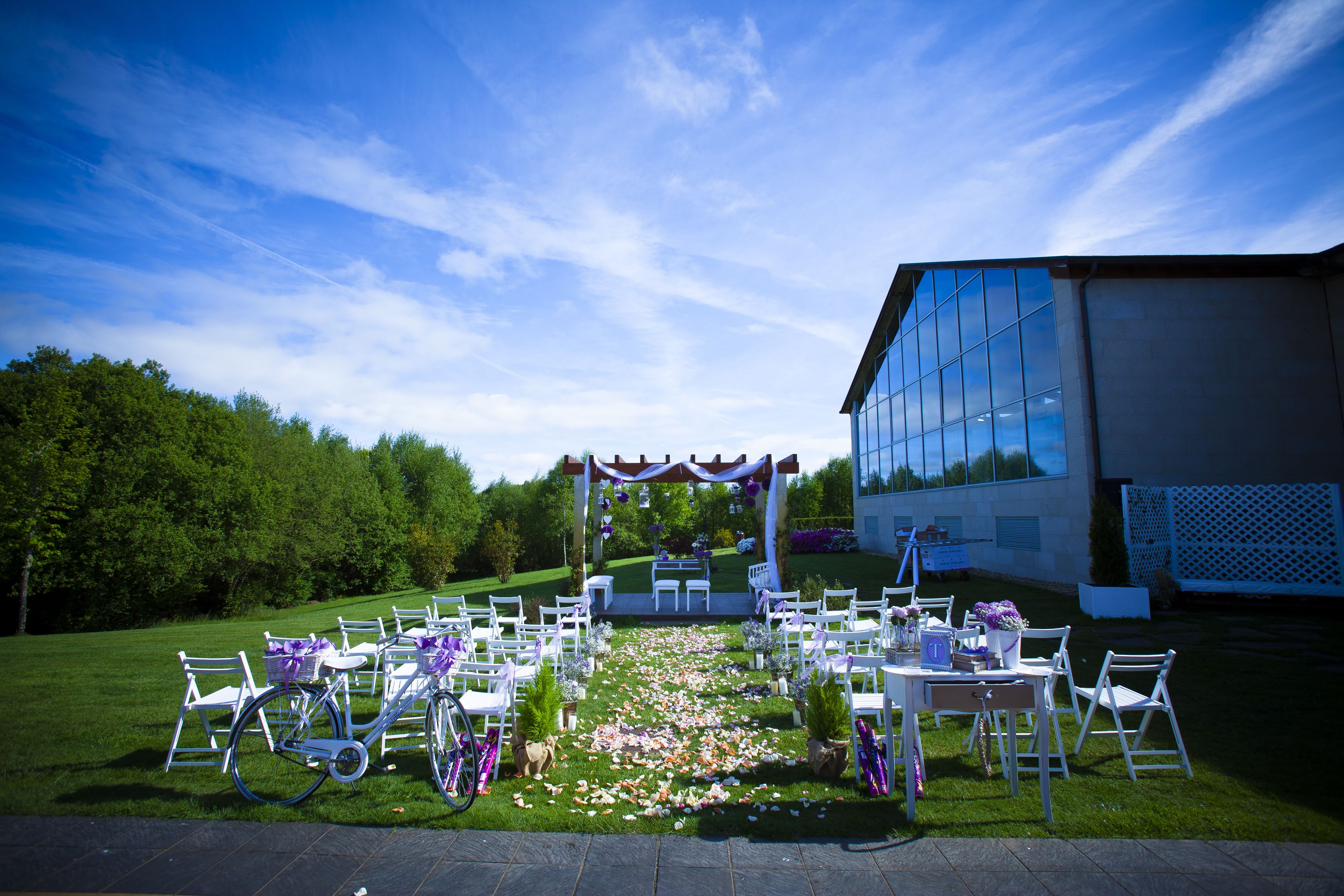 Een buitenlocatie voor een bruiloft met witte stoelen en tafels, een bloemenpad en een gebouw op de achtergrond.
