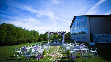 Een buitenlocatie voor een bruiloft met witte stoelen en tafels, een bloemenpad en een gebouw op de achtergrond.