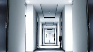 Un couloir d’hôtel avec un tapis à rayures, un éclairage encastré et des portes de part et d’autre.
