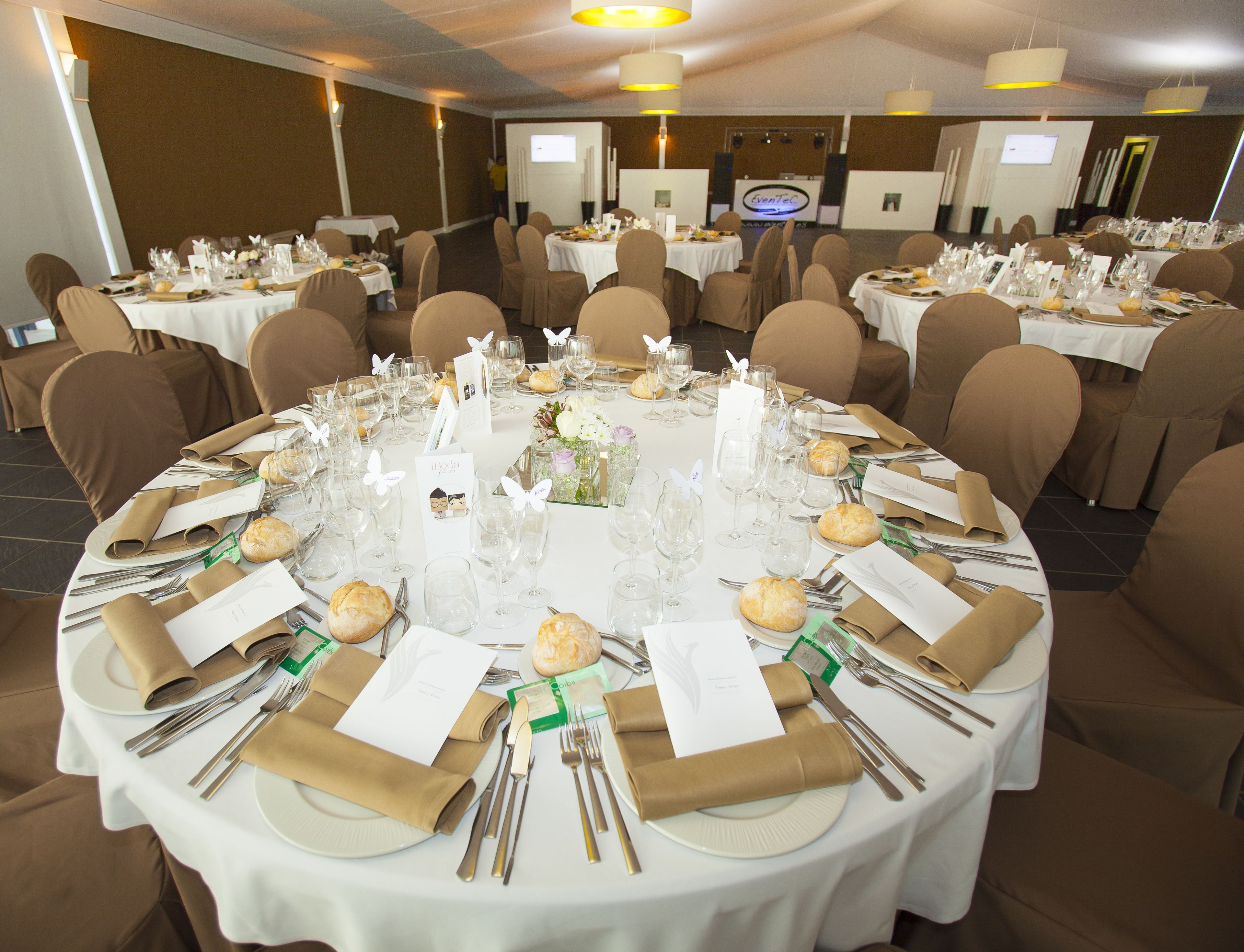 Ein Festsaal mit runden Tischen, festlich gedeckt für eine formelle Veranstaltung, inklusive Platzdeckchen, Gläsern und floralen Tischdekorationen.