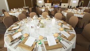 Ein Festsaal mit runden Tischen, festlich gedeckt für eine formelle Veranstaltung, inklusive Platzdeckchen, Gläsern und floralen Tischdekorationen.