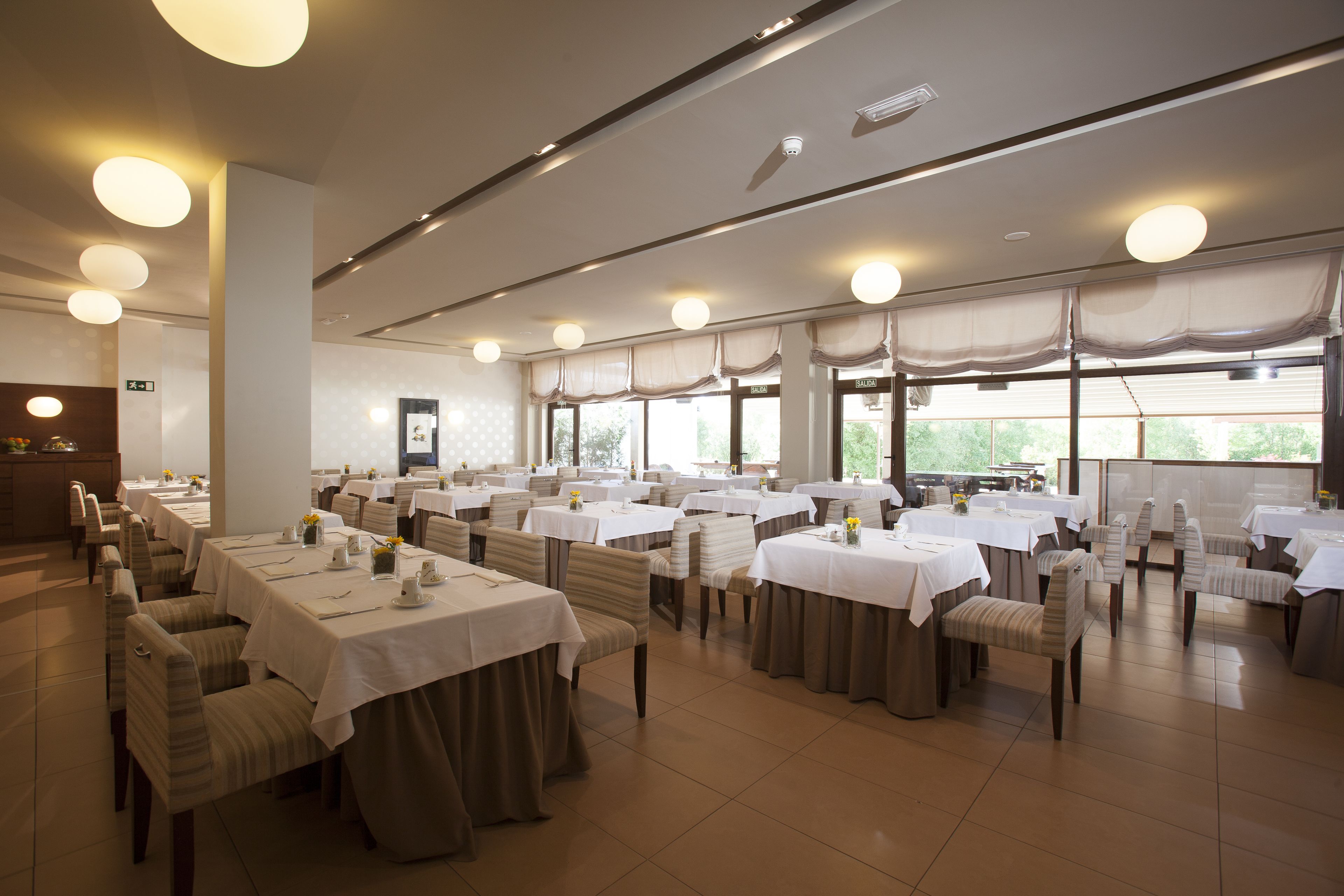 A spacious dining area with multiple tables and chairs, large windows, and a clean, modern design.