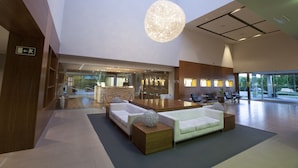 Un hall d’entrée spacieux avec un plafond haut, un grand comptoir de réception en bois et des espaces aménagés pour s’asseoir.