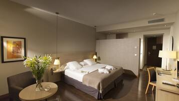 A hotel room with a bed, bedside table, lamp, chair, desk, and a vase with flowers.