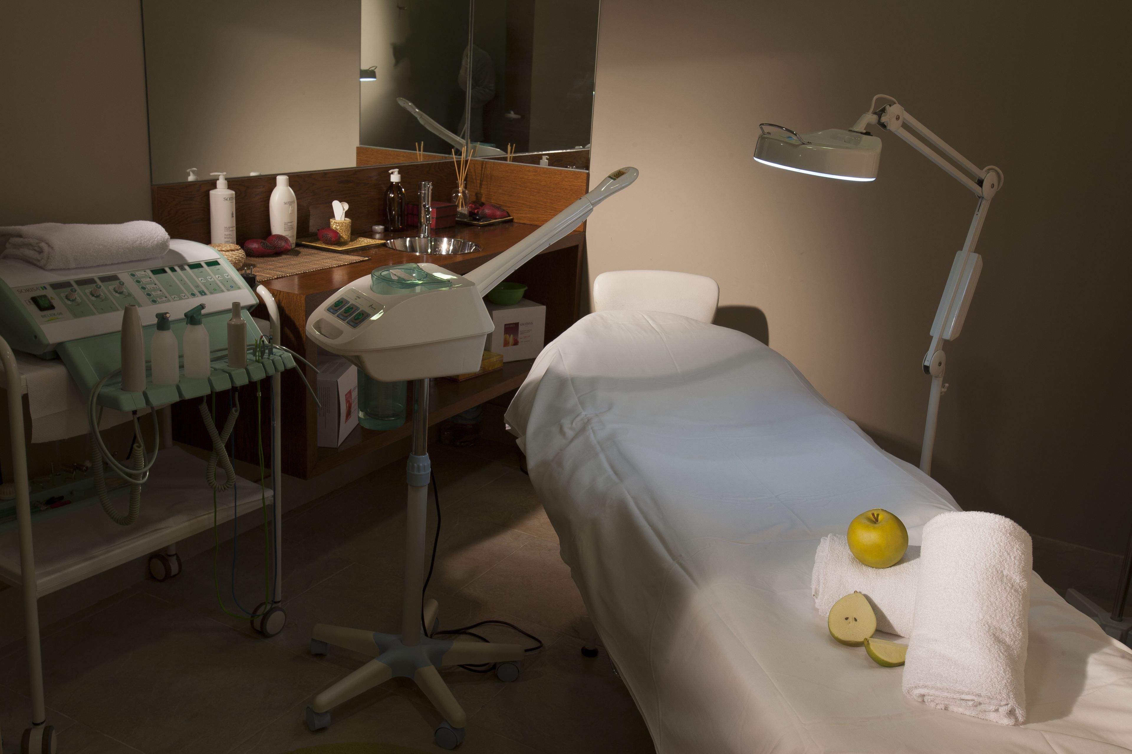 Un consultorio médico con una cama, camilla de exploración, equipo médico y una lámpara.