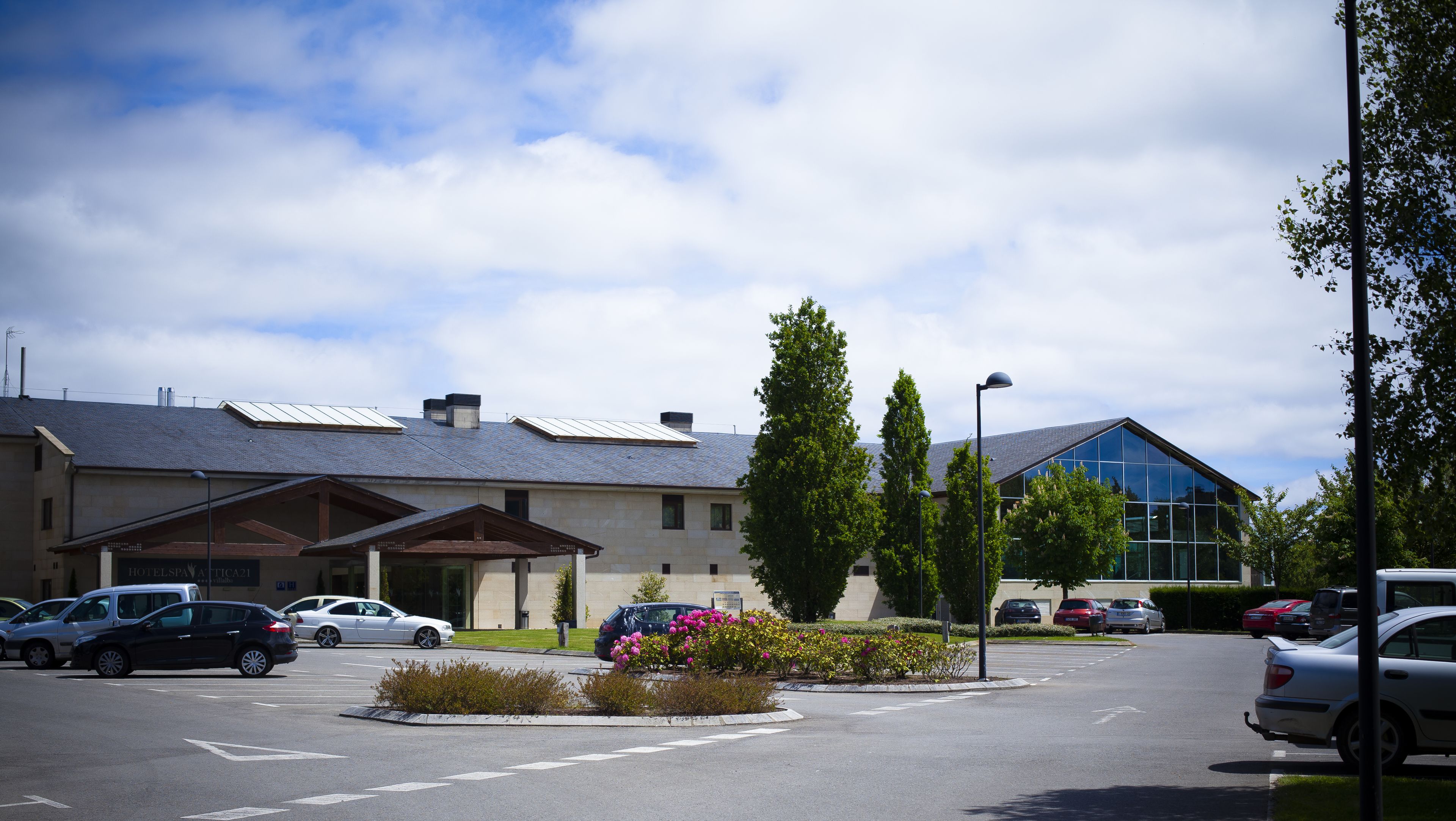 A hotel with a parking lot, several cars, and a building with a modern design.