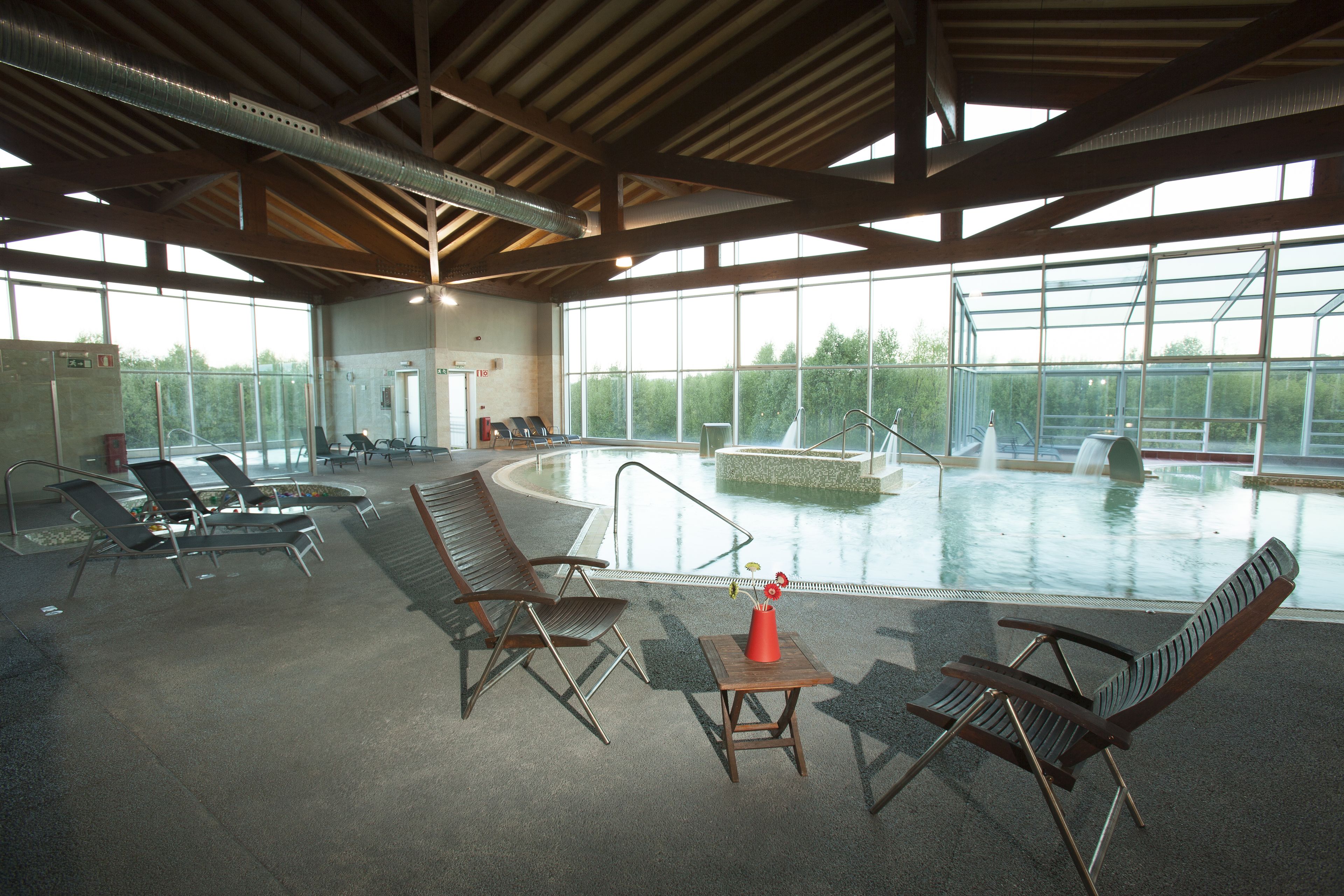 An indoor swimming pool area with lounge chairs and a small table with a vase.