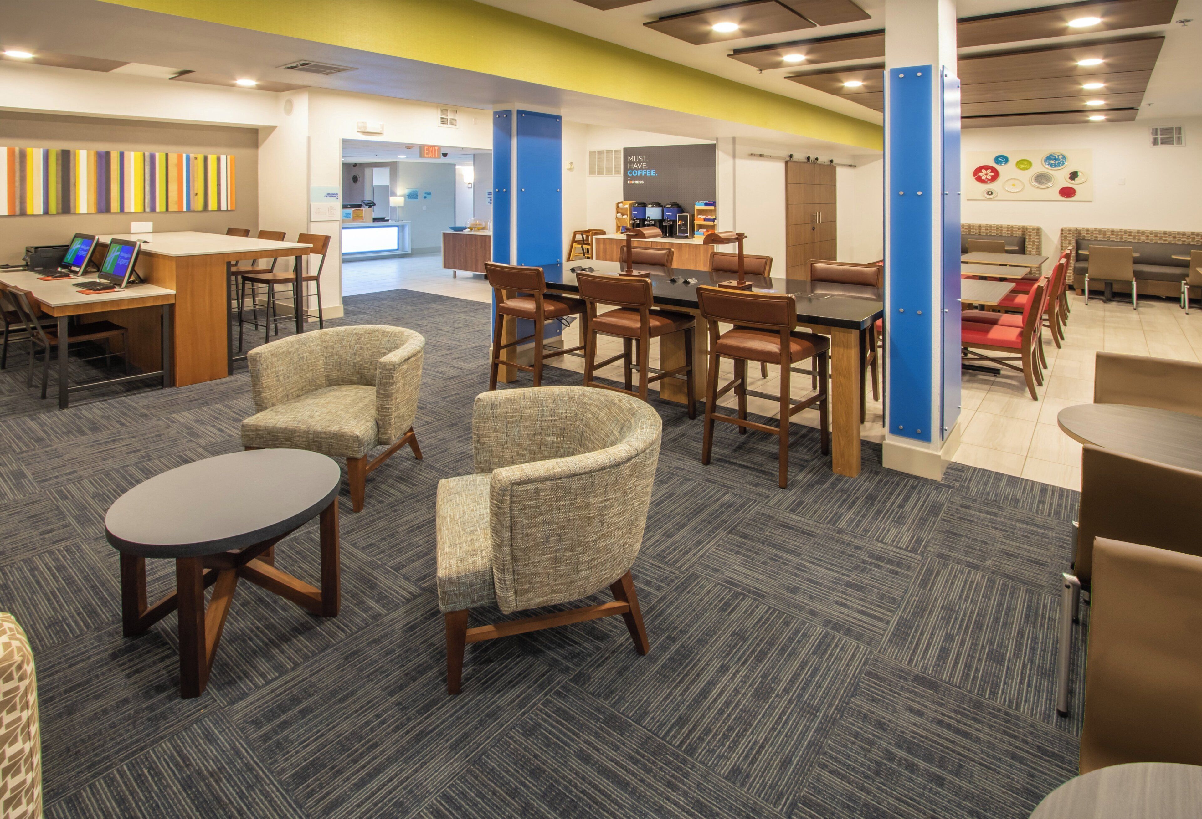 A modern office space with a mix of seating arrangements, including chairs and tables, and a reception area with a coffee station.