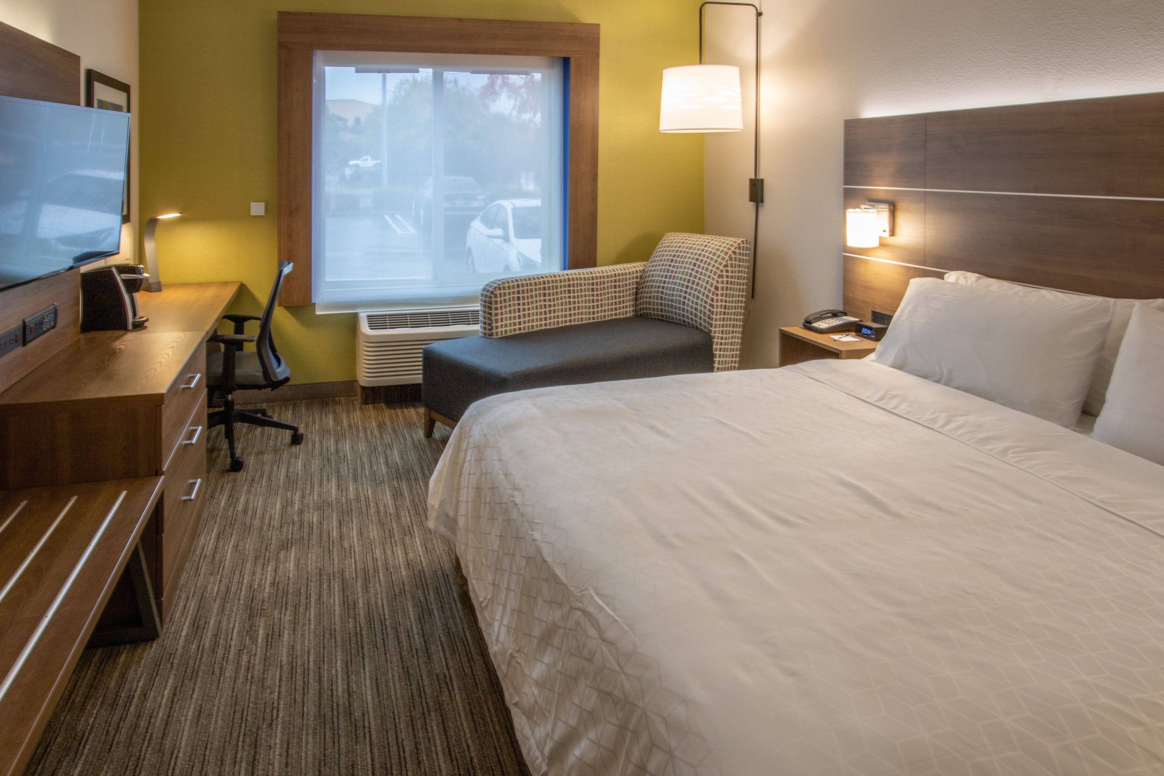 A hotel room with a large bed, a desk with a chair, a television, and a window with a view of the outside.