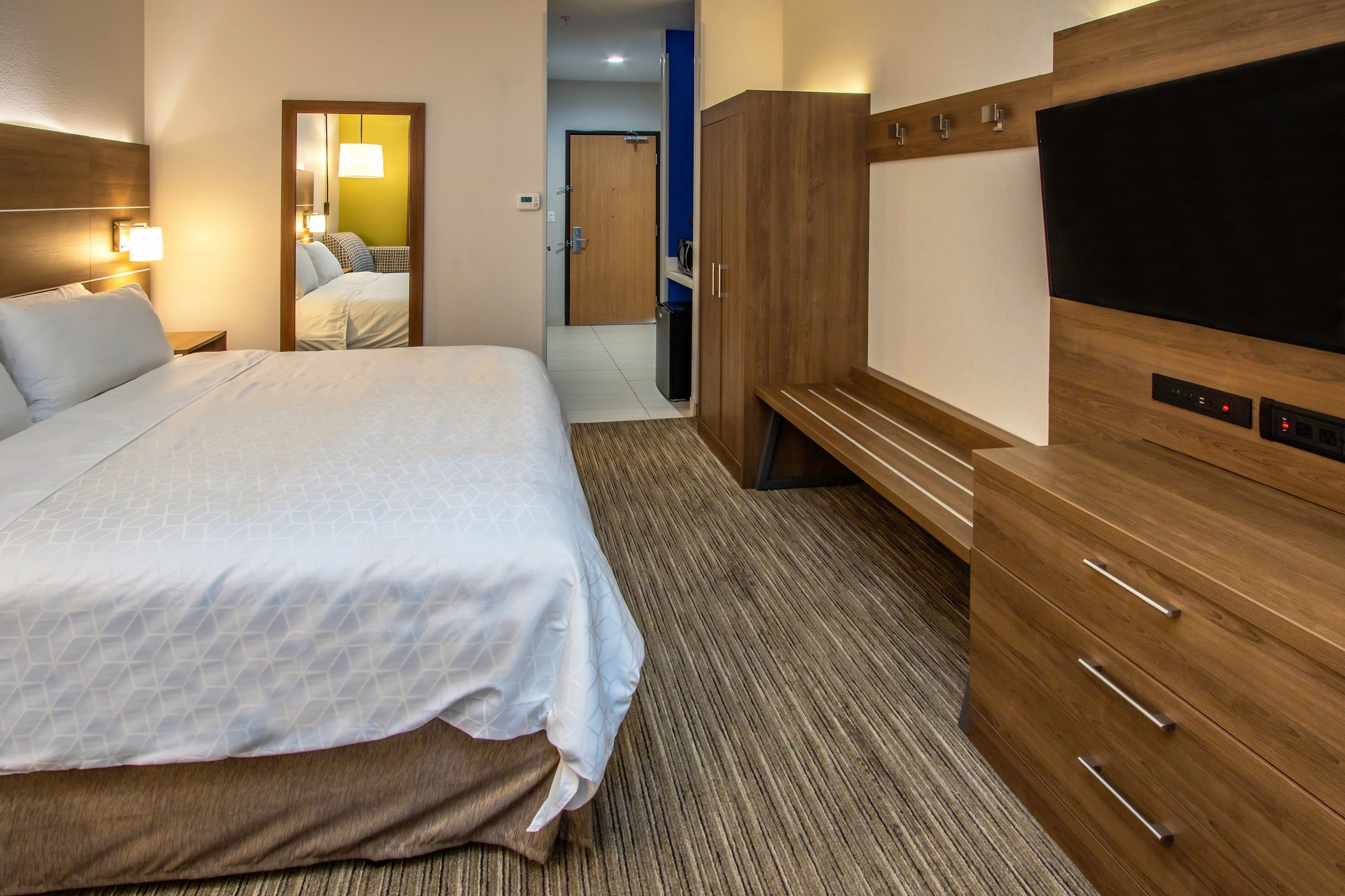 A hotel room with a bed, a TV, a wardrobe, and a mirror.