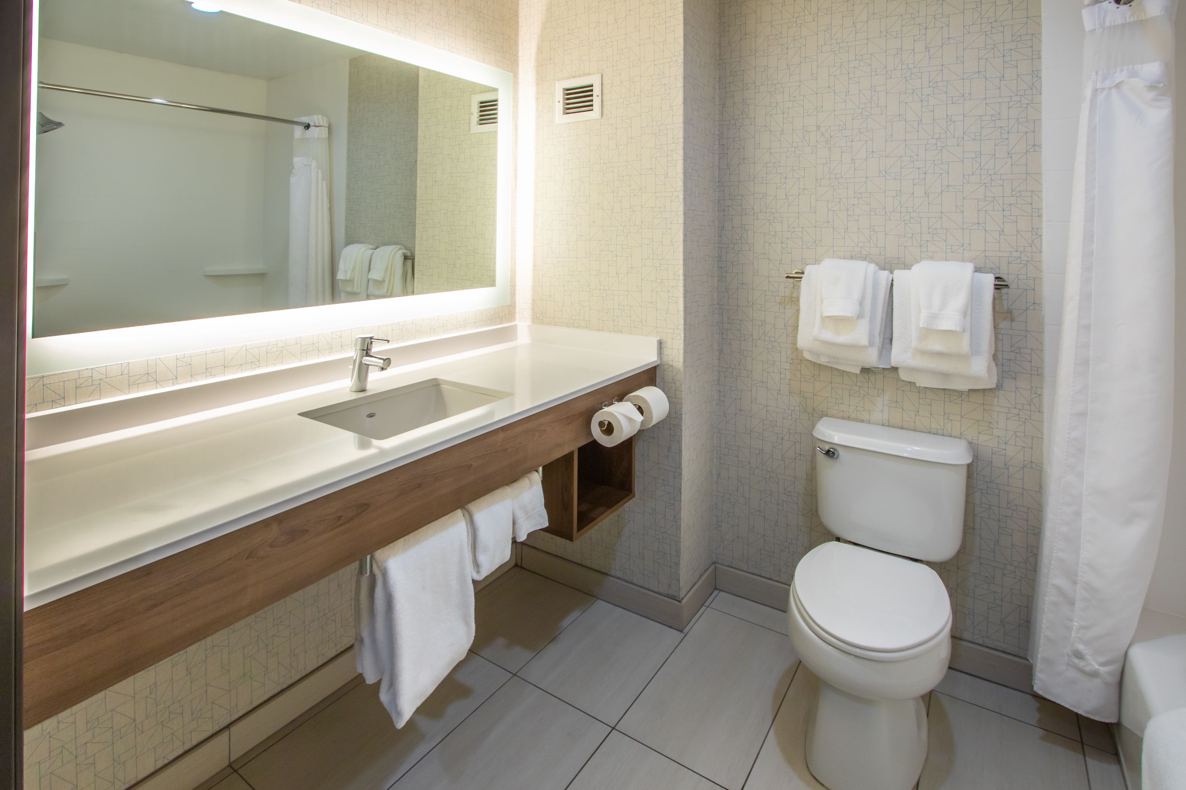 A modern bathroom with a large mirror, a sink, a toilet, and a shower curtain.