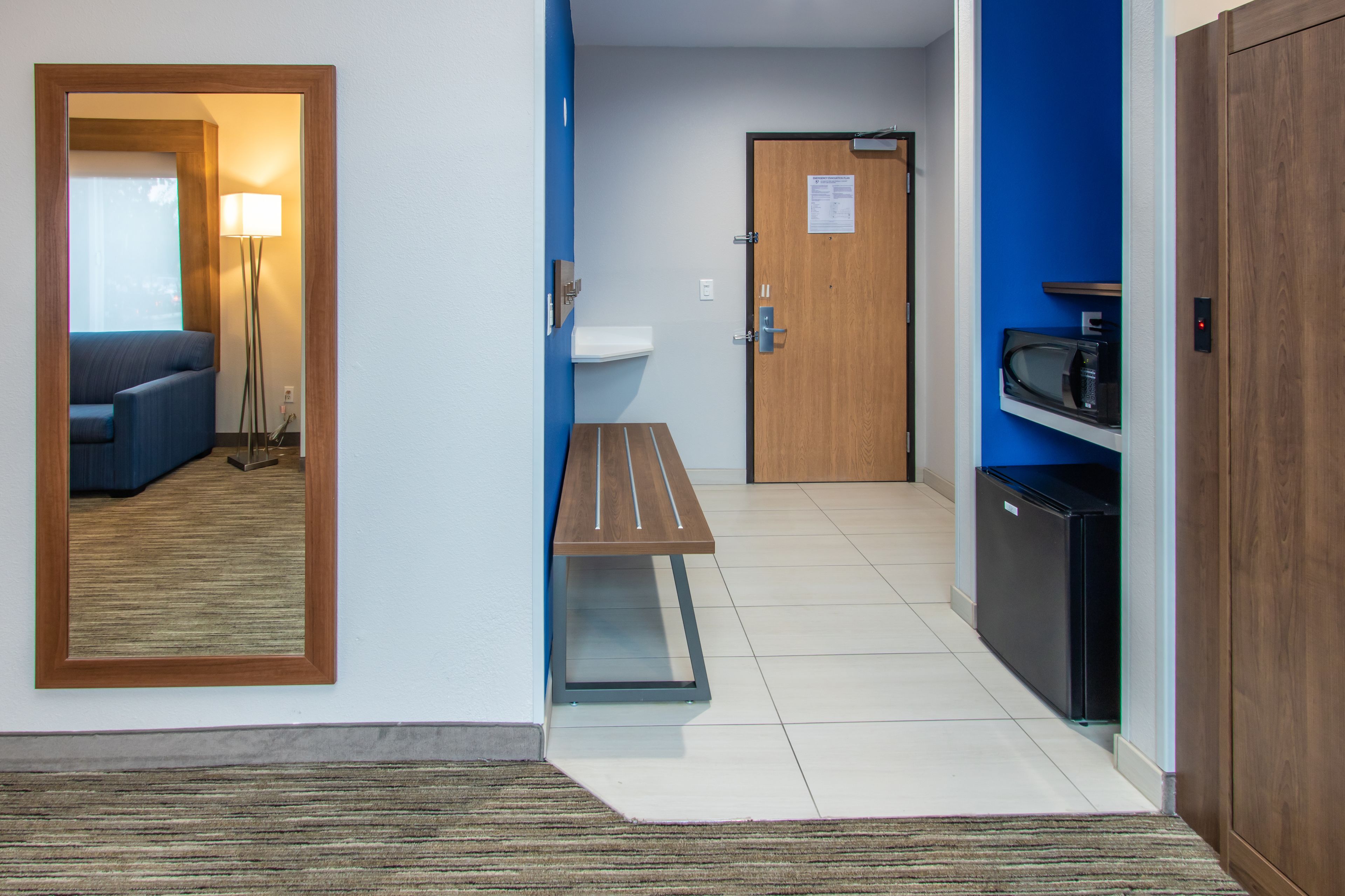Habitación de hotel con un banco de madera, un lavamanos, un microondas y una puerta con un letrero.