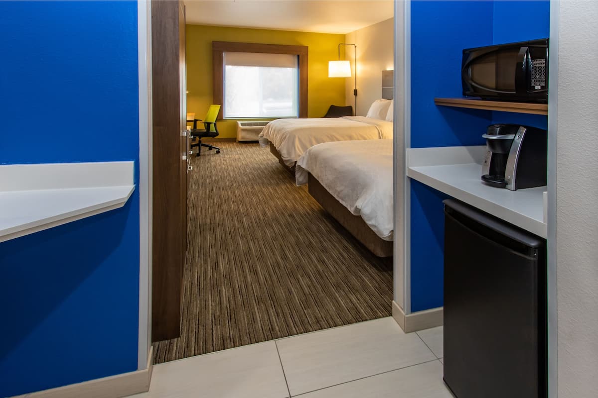 A hotel room with two beds, a desk, a chair, a microwave, and a coffee maker.