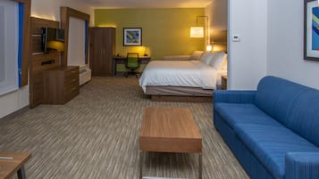 A hotel room with a bed, a blue sofa, a wooden desk, a chair, a TV, and a framed picture on the wall.