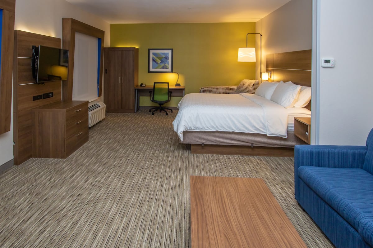 A hotel room with a bed, a desk, a chair, a TV, and a blue sofa.