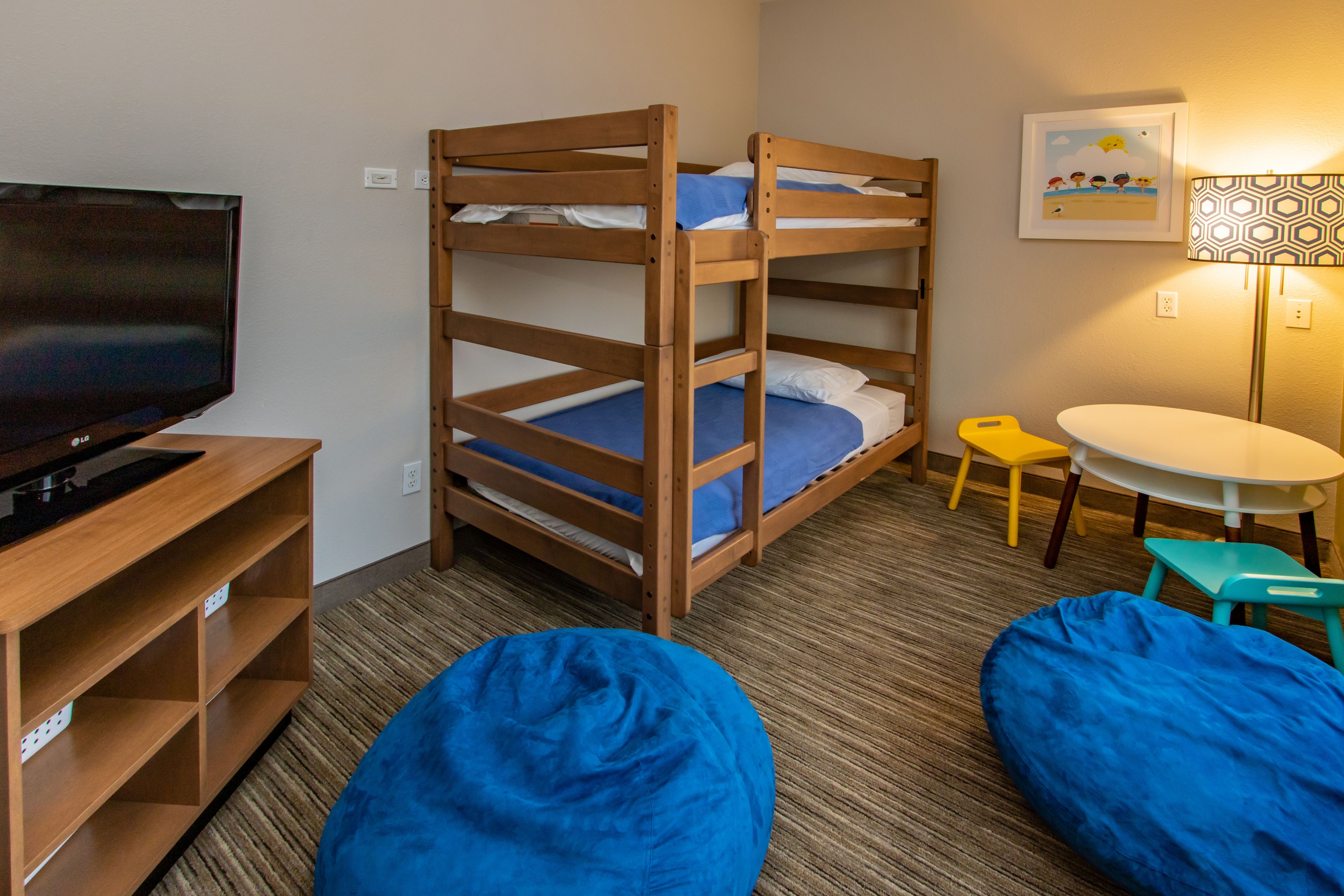 A bunk bed with a TV, a small table, and two bean bags in a room with a carpeted floor.