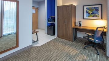 A hotel room with a desk, chair, kitchenette, and a framed picture on the wall.