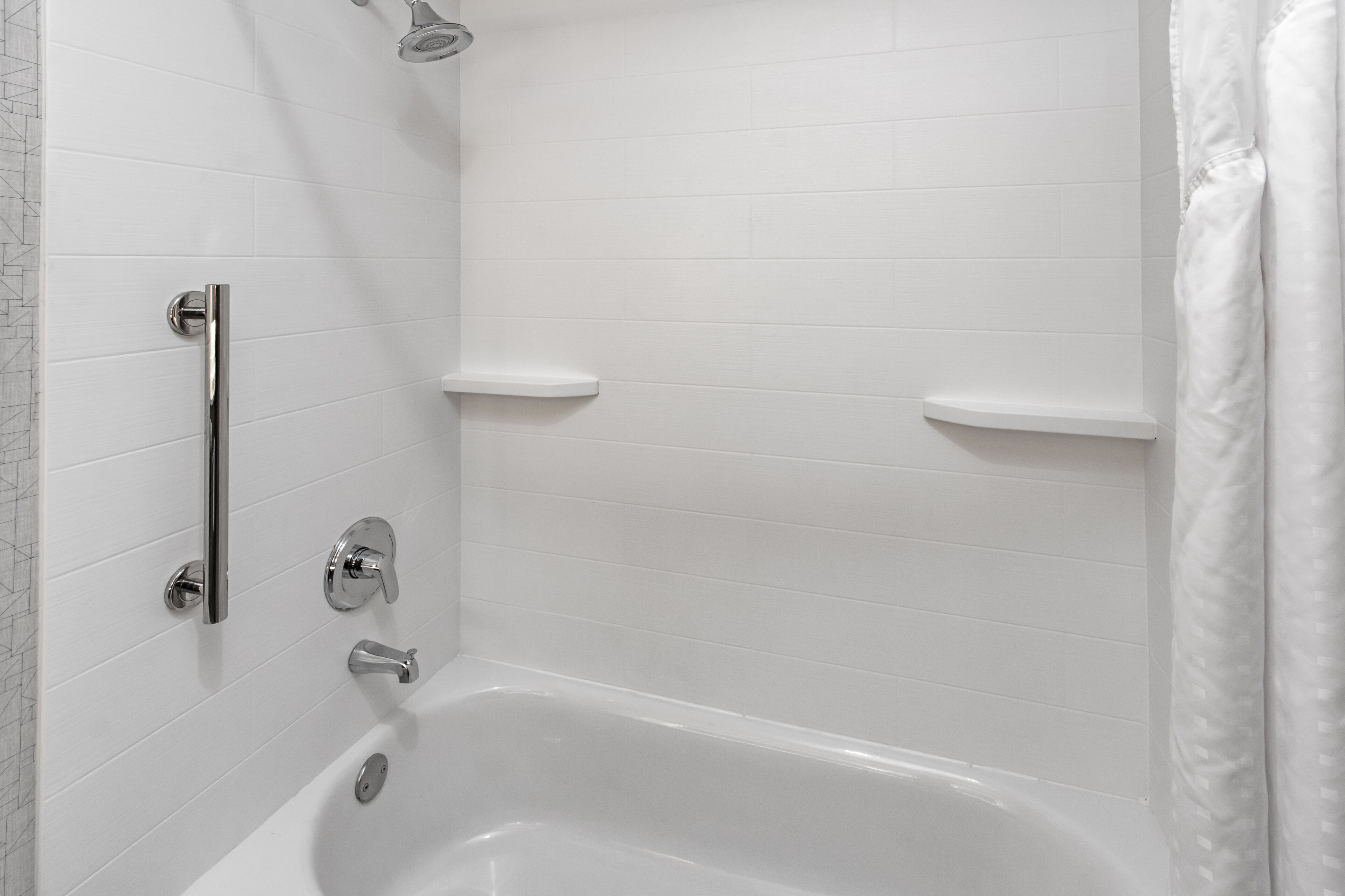 A modern bathroom with a bathtub, a shower, and a handrail.