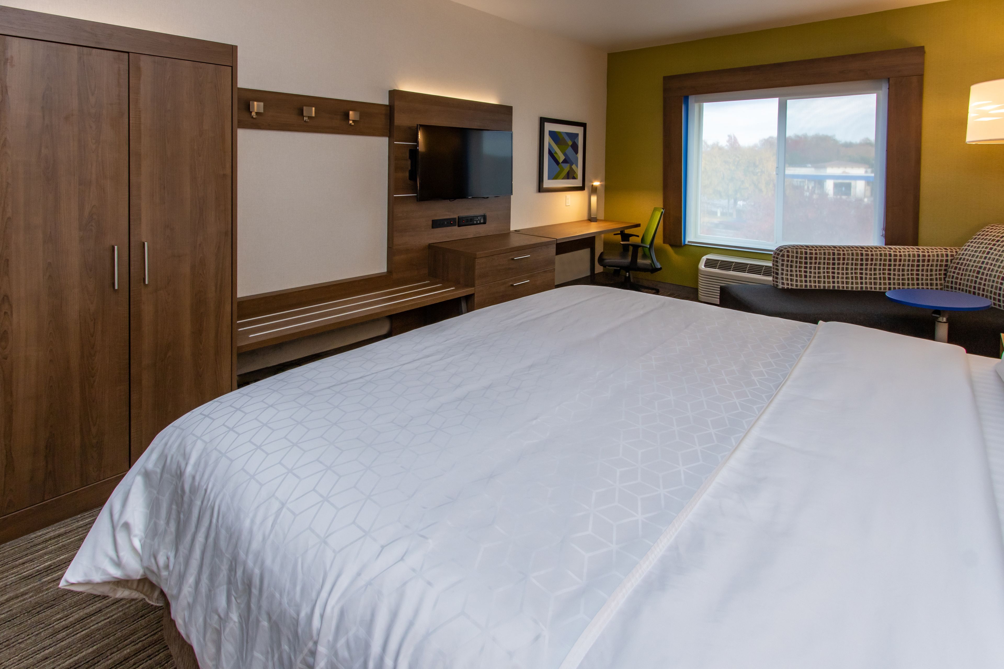 A hotel room with a large bed, a desk with a chair, a television, and a window with a view.