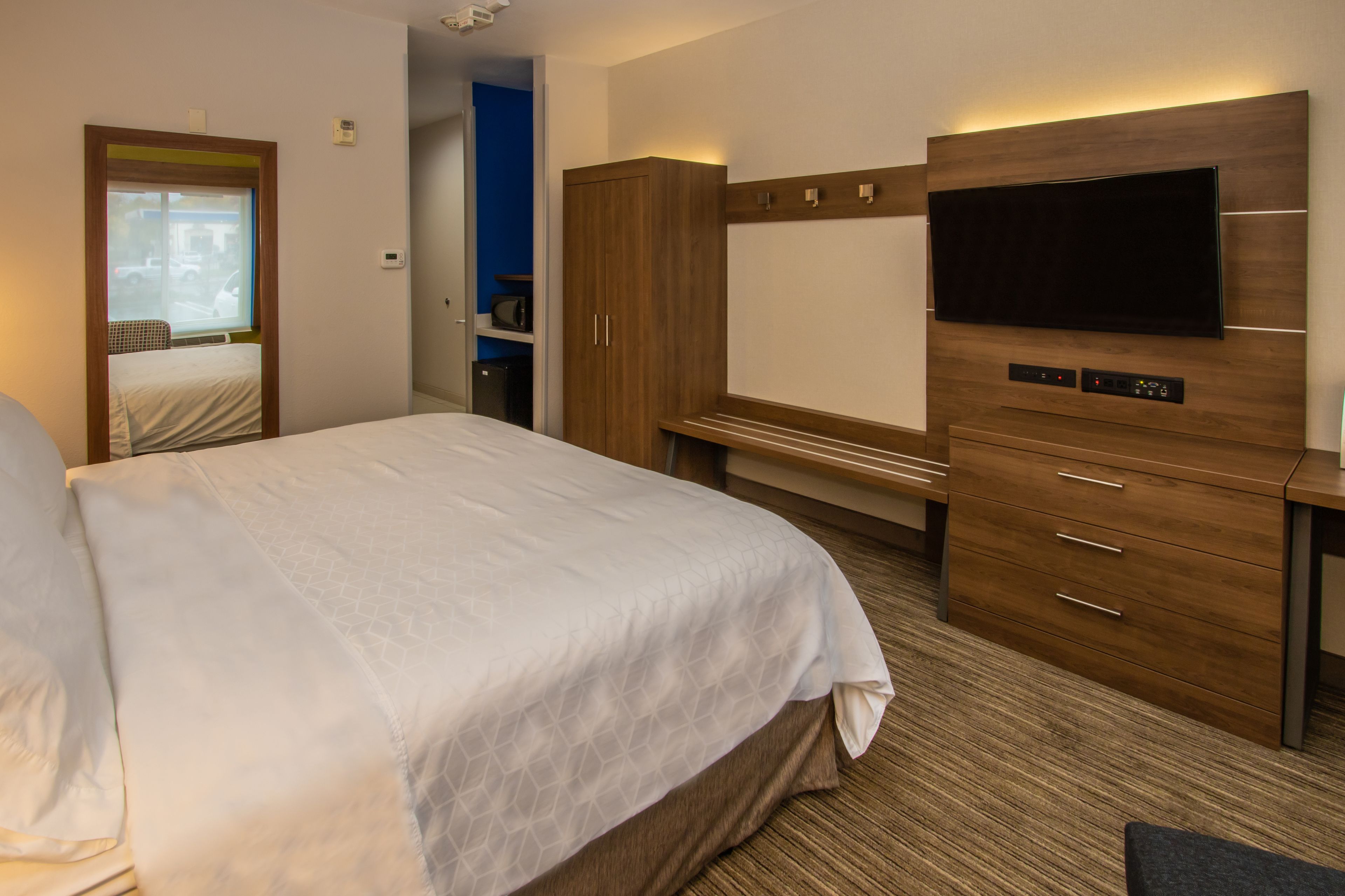 A hotel room with a large bed, wooden wardrobe, a flat-screen TV mounted on the wall, and a small desk.