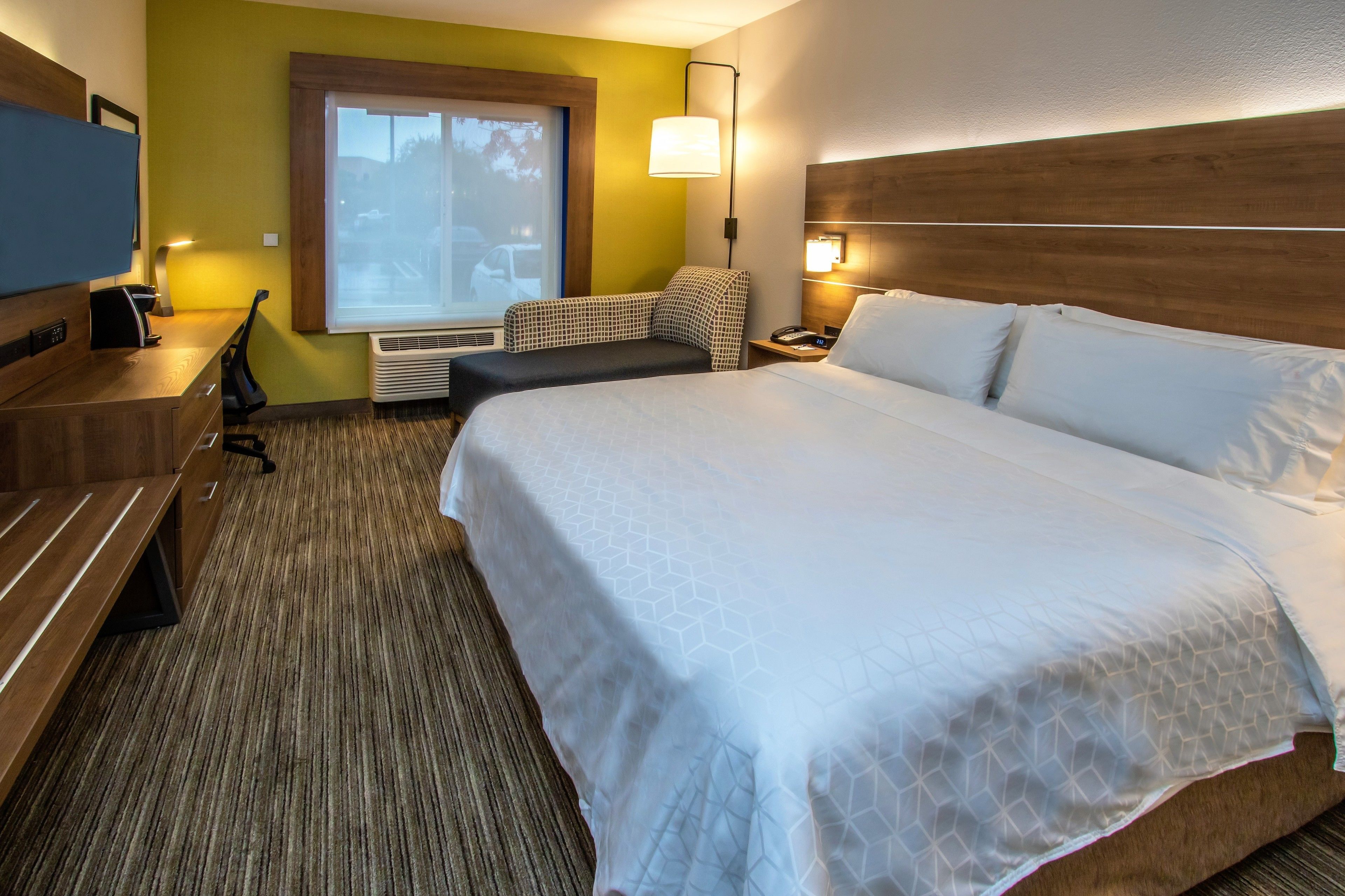 A hotel room with a large bed, a desk with a chair, a TV, and a window with a view of the outside.