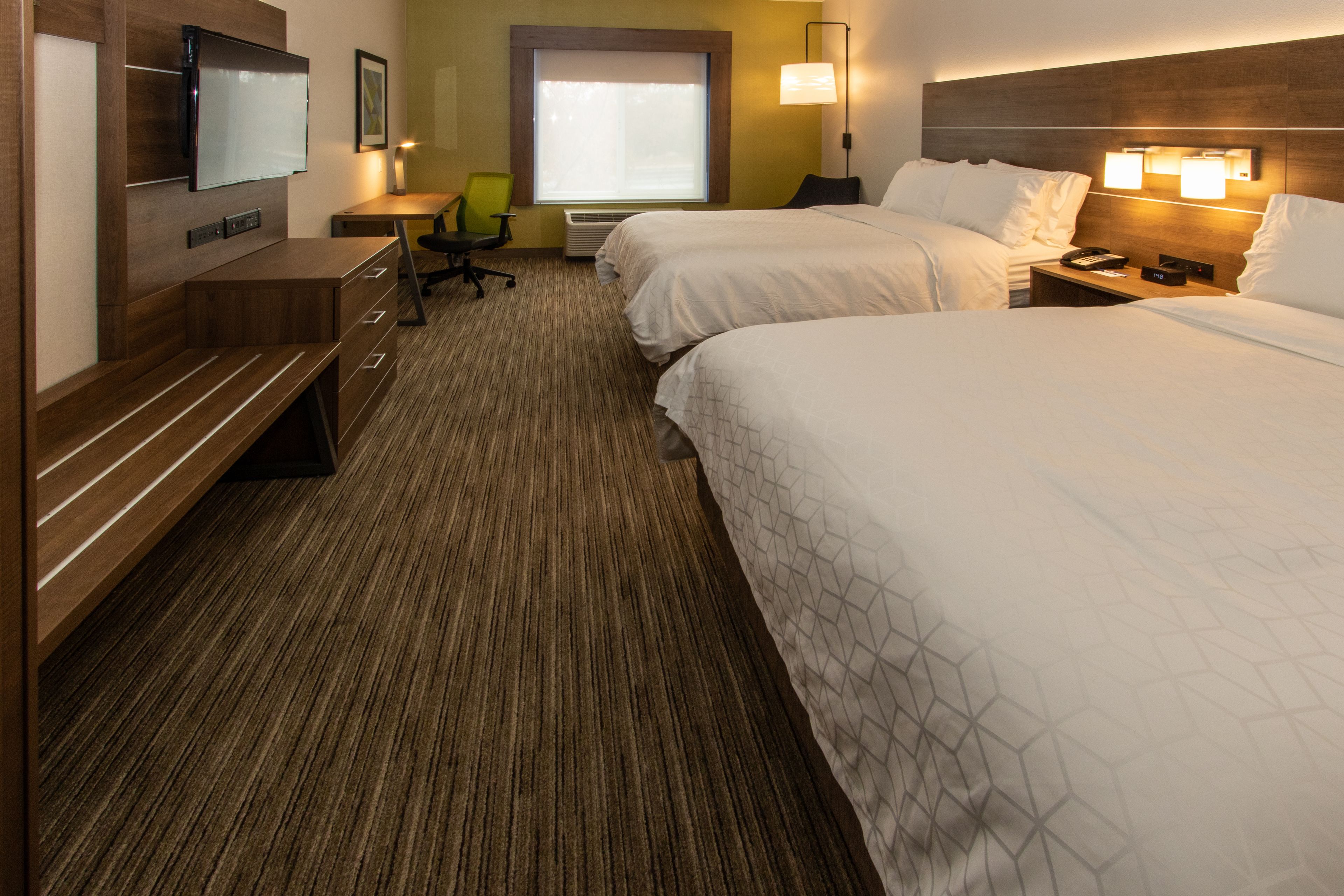 A hotel room with two beds, a desk, a chair, a TV, and a window with blinds.