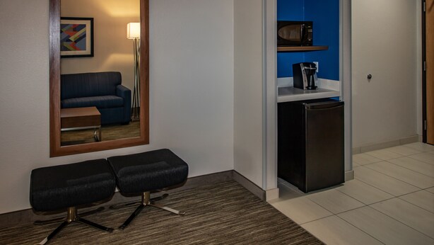 Habitación de hotel con un espejo de marco de madera, un sofá azul, un escritorio pequeño negro, un refrigerador negro y un microondas en un estante azul.