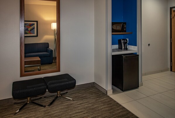 Habitación de hotel con un espejo de marco de madera, un sofá azul, un escritorio pequeño negro, un refrigerador negro y un microondas en un estante azul.