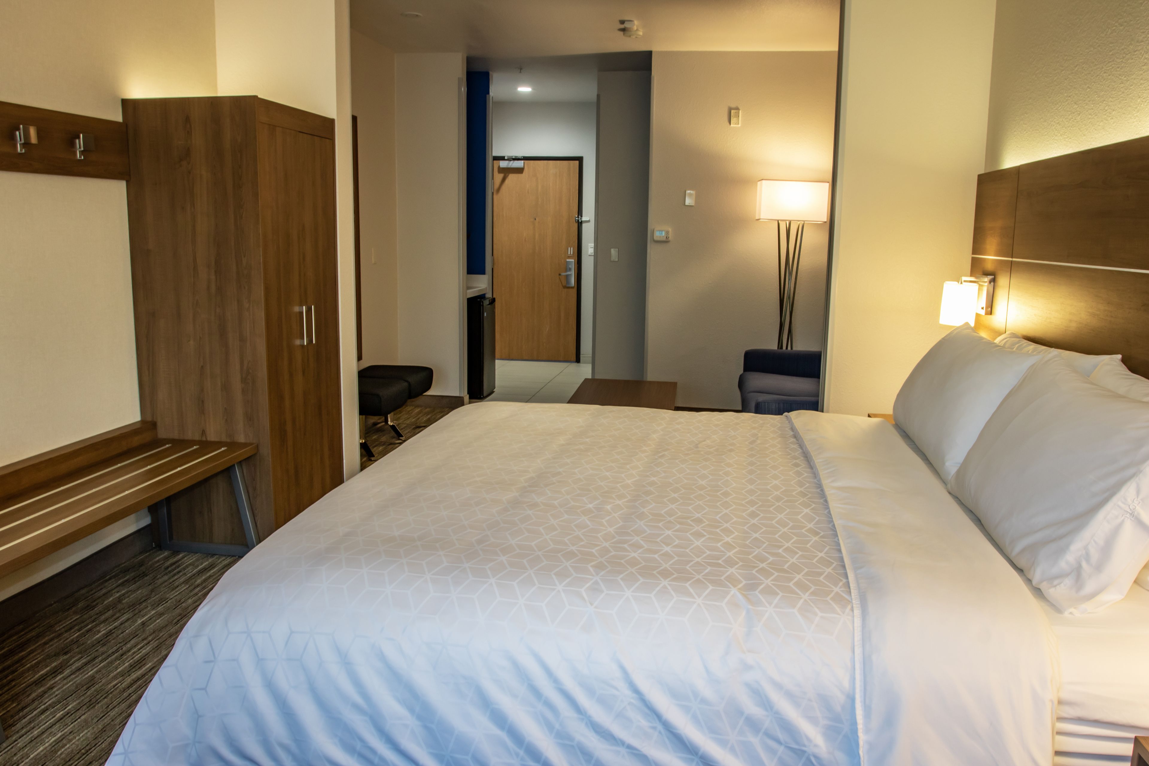 A hotel room with a large bed, a wooden wardrobe, a desk, and a mirror.