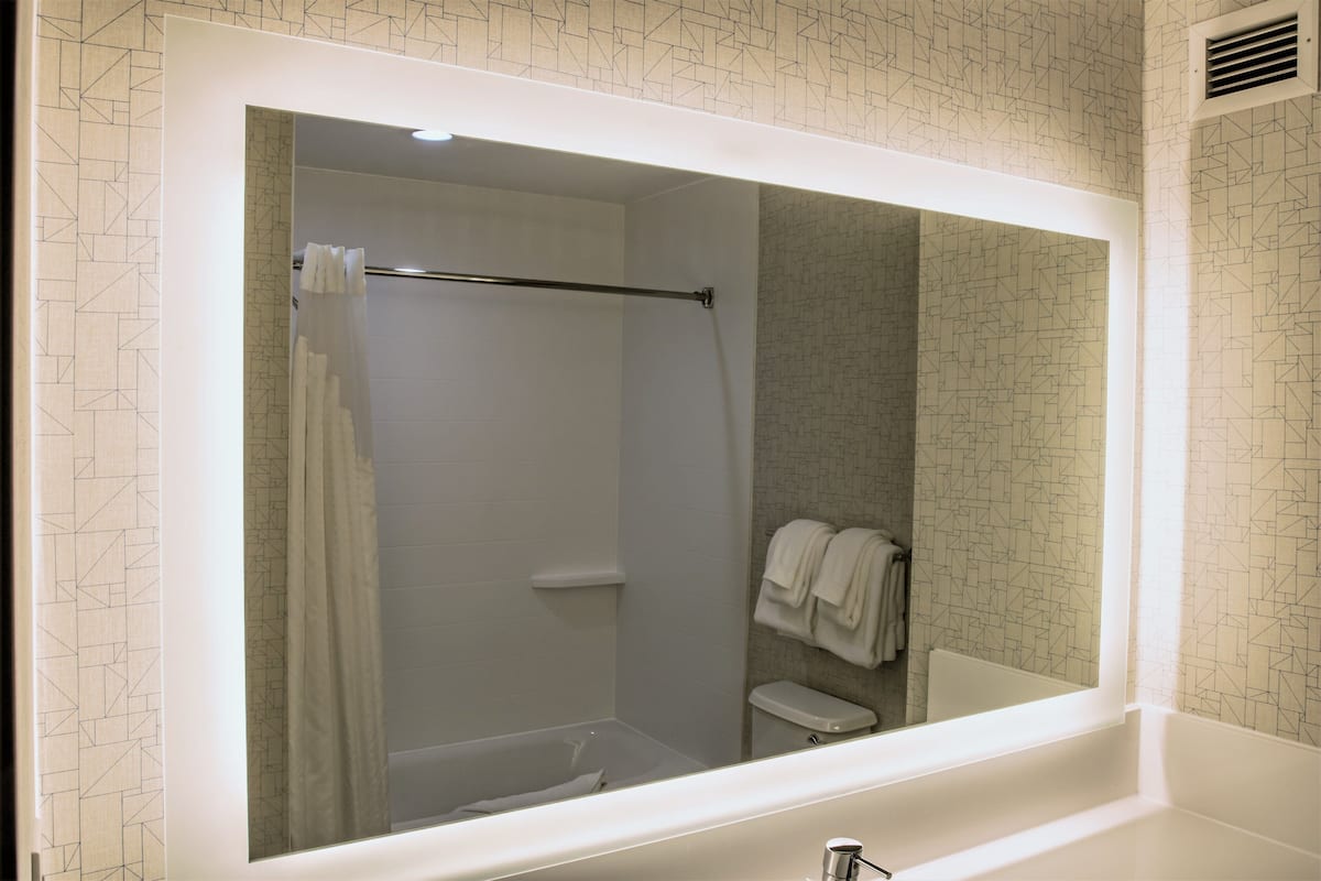 A bathroom with a large mirror, a bathtub, a shower area, and a toilet.