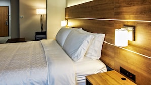 Una habitación de hotel con cabecera de madera, cama con sábanas blancas y dos lámparas de pared.
