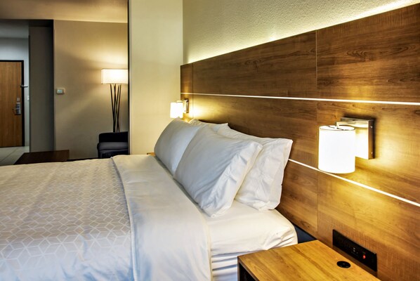 A hotel room with a wooden headboard, a bed with white linens, and two wall-mounted lamps.
