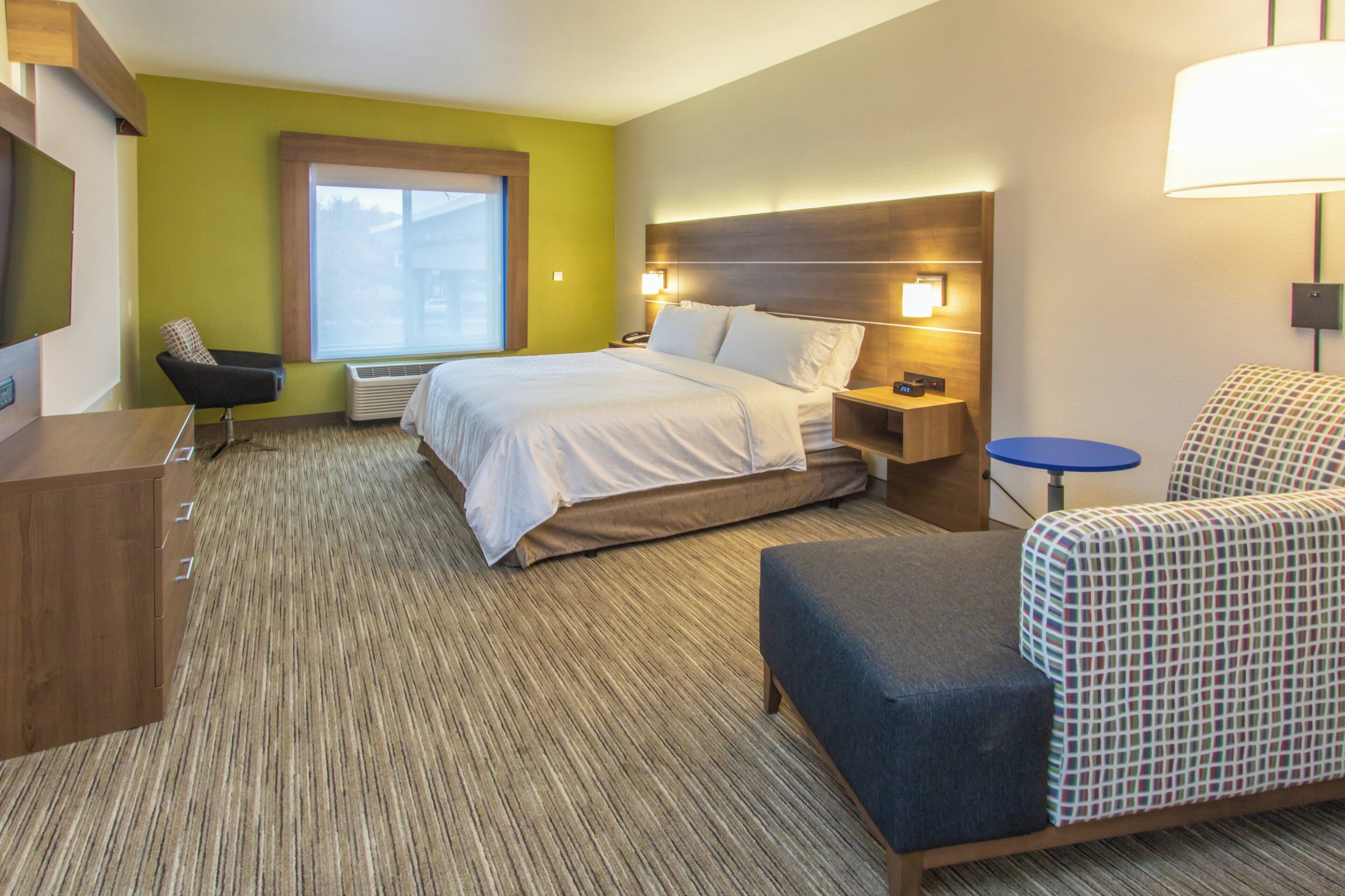 Una habitación de hotel con cama, mesita de noche, silla y una pequeña mesa con lámpara.