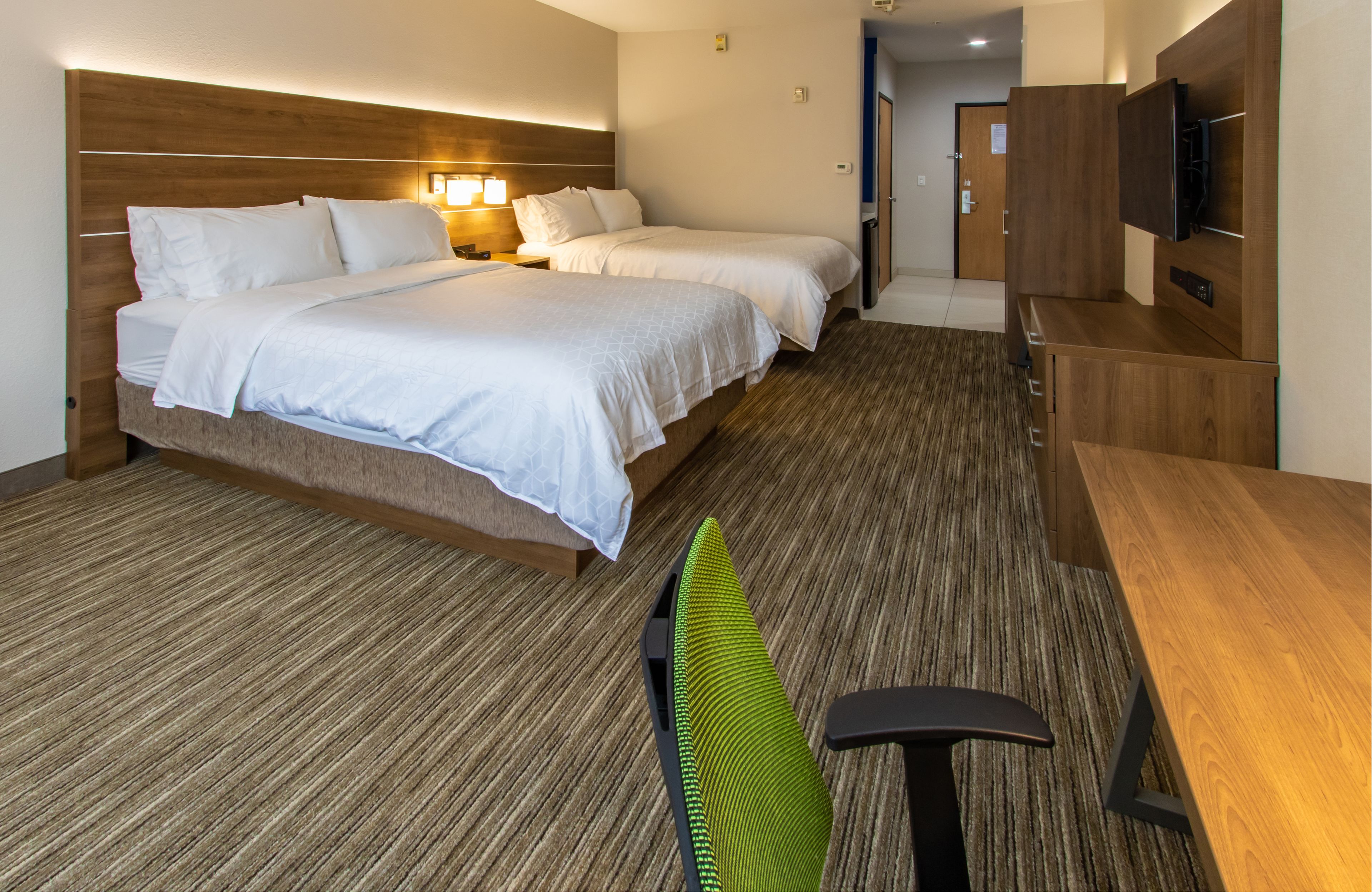 A hotel room with two beds, a desk, a chair, a TV, and a wooden headboard.