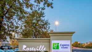 Señal de hotel con la marca 'Roseville' y 'Express & Suites', rodeada de vegetación y un estacionamiento.