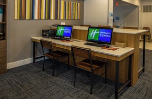 Un mostrador de recepción con dos monitores de ordenador mostrando el logotipo de Holiday Inn Express, una impresora y un conjunto de sillas.
