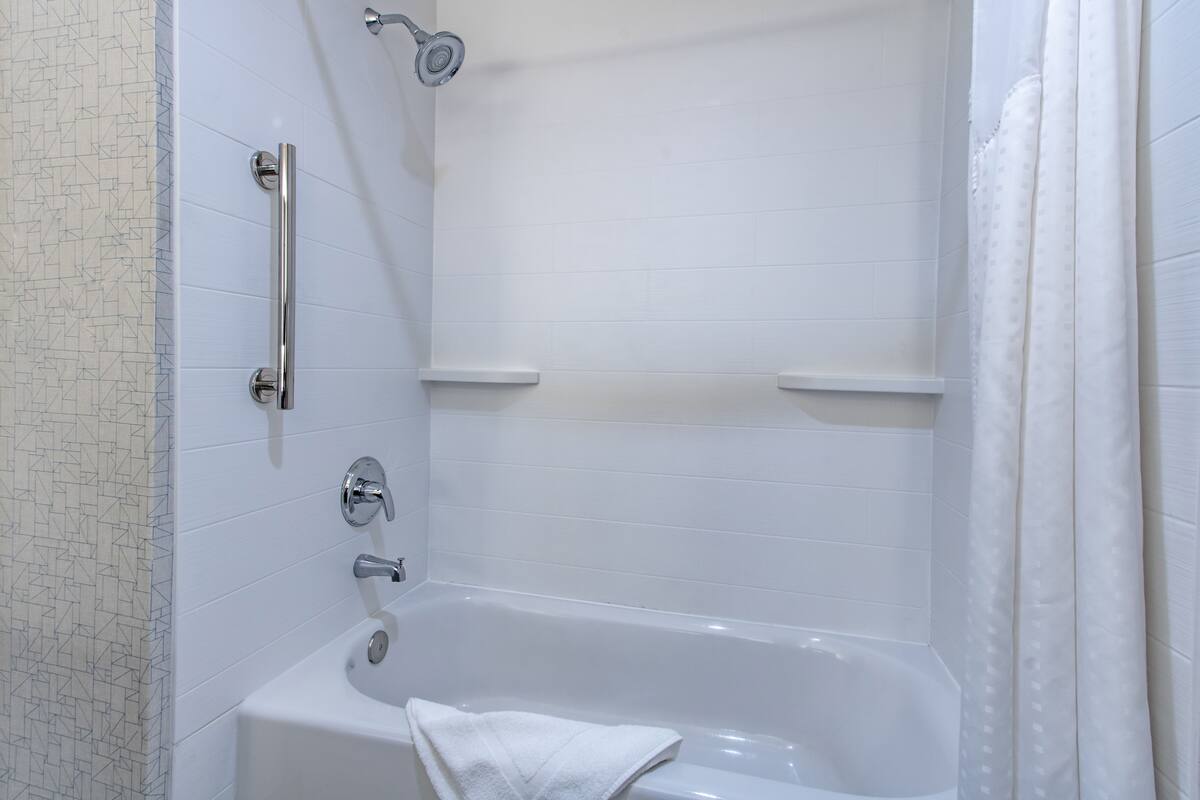 A modern bathroom with a bathtub, a handheld showerhead, and a towel rack.