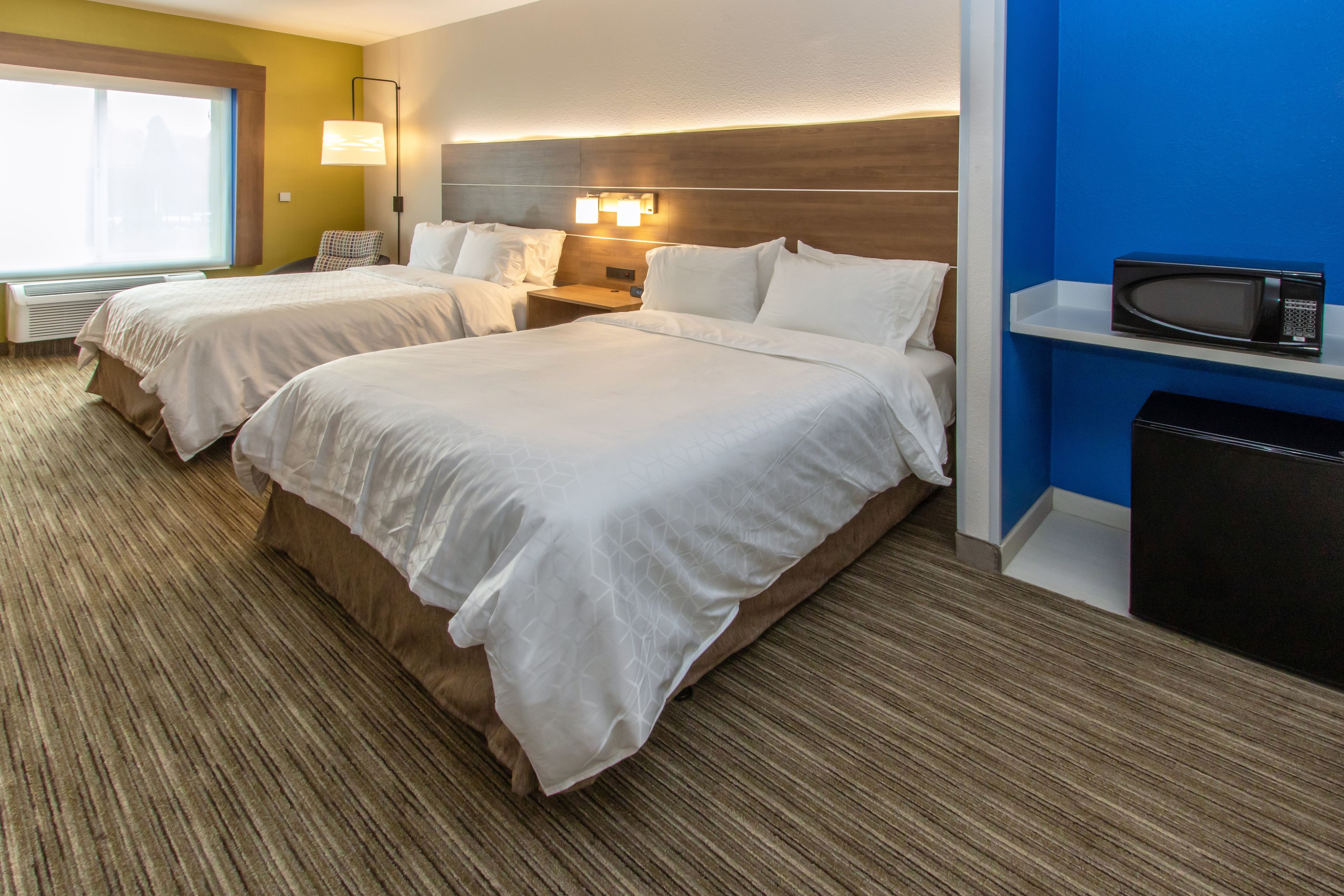 A hotel room with two beds, a microwave, and a TV on a shelf.
