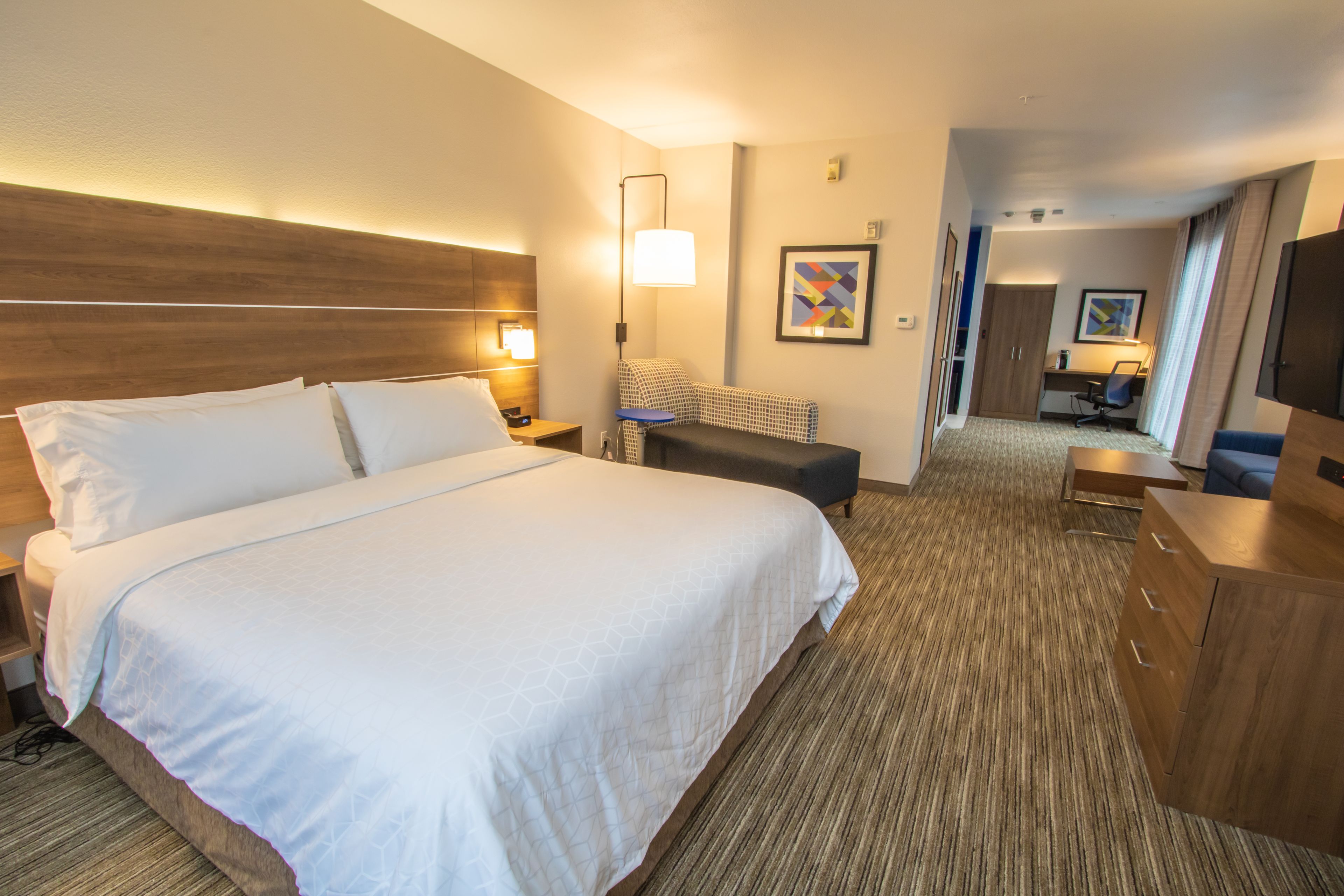 A hotel room with a large bed, a desk, a chair, a TV, and a wardrobe.