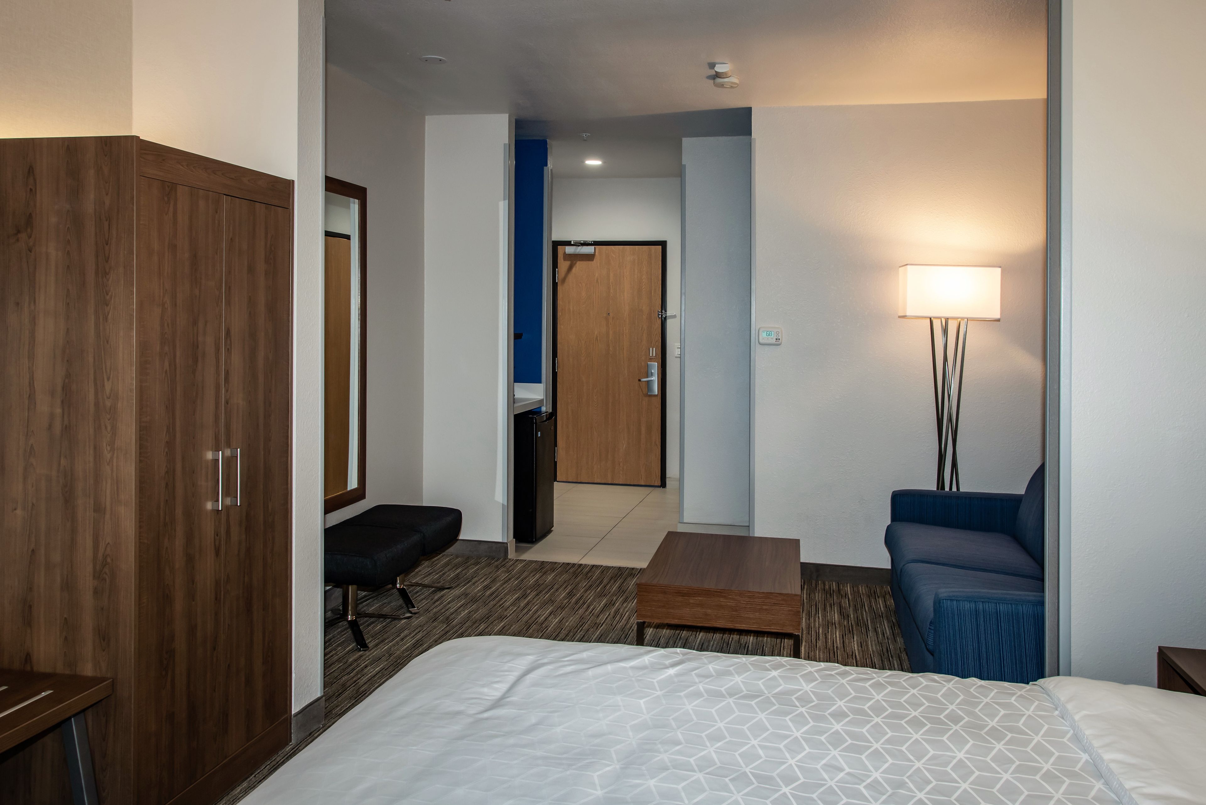 A hotel room with a bed, a desk, a chair, a wardrobe, and a bathroom visible through an open door.
