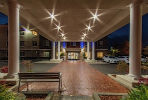 A hotel entrance with a covered walkway, columns, and a bench.