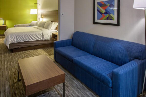 A hotel room with a bed, a blue sofa, a wooden table, and a framed abstract painting on the wall.
