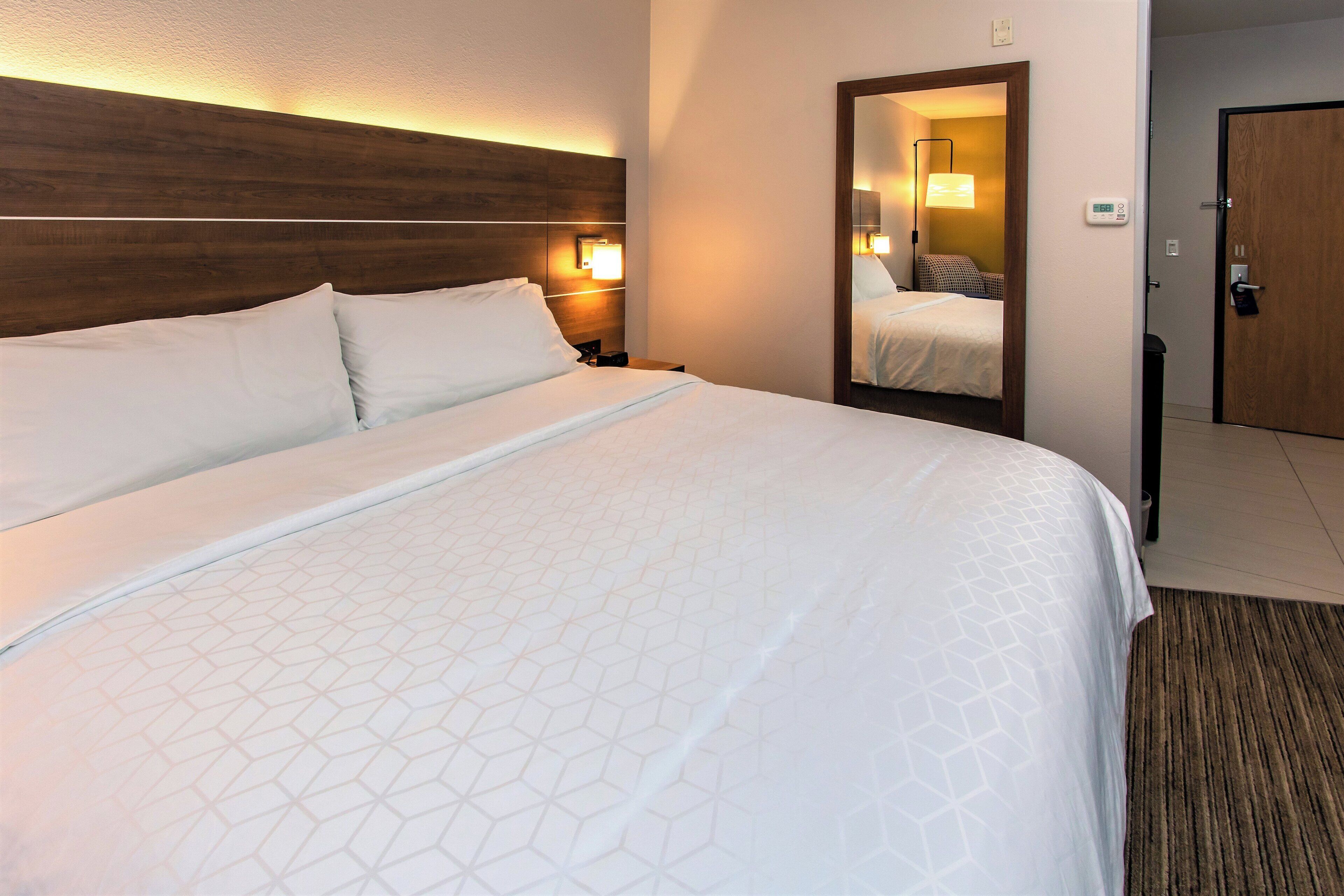 A hotel room with a large bed, a wooden headboard, a nightstand, a bedside lamp, and a mirror.