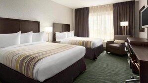 A hotel room with two beds, a desk, a chair, a TV, and a window with curtains.