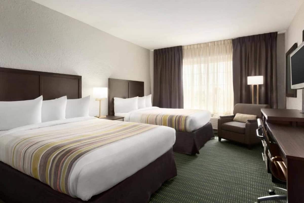 Ein Hotelzimmer mit zwei Betten, einem Schreibtisch, einem Stuhl, einem Fernseher und einem Fenster mit Vorhängen.