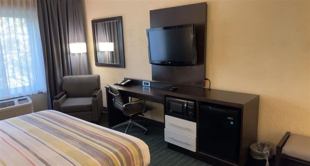 Habitación de hotel con cama, escritorio con computadora, silla, televisor y ventana con cortinas.