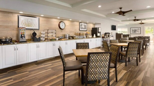 A spacious dining area with multiple tables and chairs, a kitchen area with white cabinets, and ceiling fans.