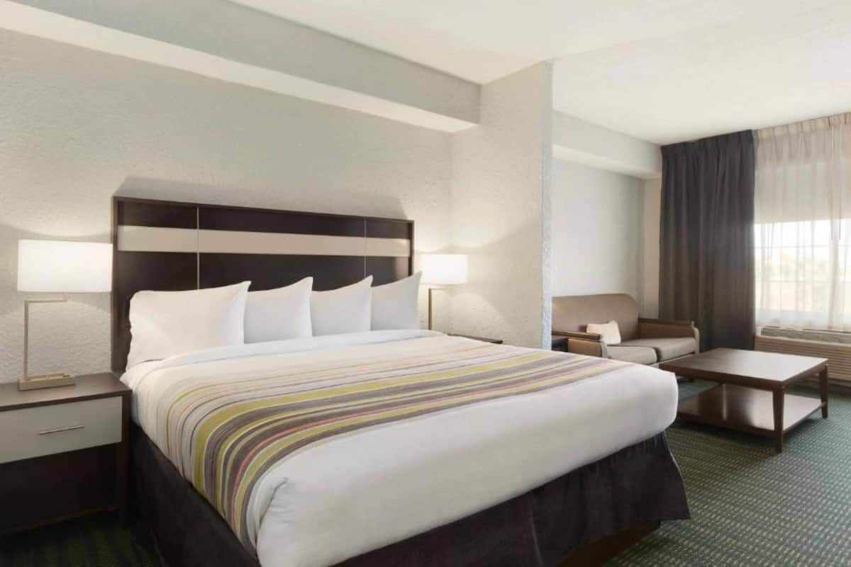 Ein Hotelzimmer mit einem großen Bett, Nachttischen, einem Sofa, einem Couchtisch und einem Fenster mit Vorhängen.