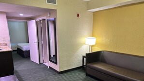 A hotel room with a green carpet, a brown sofa, a lamp, and a bed with a white headboard.